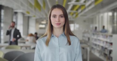 Modern ofis alanında gülümseyen stajyer kız. Ciddi bir yüzle kameraya bakan hırslı genç kadın ofis çalışanının portresi. İnsan ve kariyer kavramı. Geçmişi bulanık..