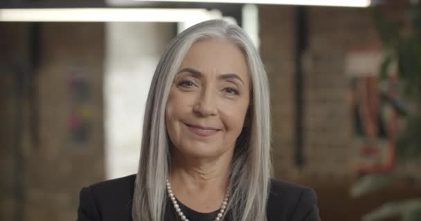 Primer plano de atractiva mujer anciana emprendedora mirando a la cámara y sonriendo. Mujer de negocios segura de mediana edad de pie y cruzando las manos. Retratos. Antecedentes . — Vídeo de stock