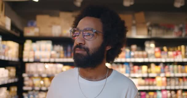 Zbliżenie przystojnego mężczyzny w okularach spacerującego i rozglądającego się po supermarkecie. Dojrzały facet w 30s szuka produktów podczas robienia zakupów w sklepie spożywczym.Niewyraźne tło. — Wideo stockowe