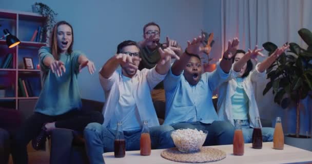 Podekscytowana grupa przyjaciół wiwatująca podczas fali, aplikująca siedząc przed telewizorem. Szczęśliwi ludzie wspierający zespół, dając przybicie piątki i bawiąc się podczas oglądania sportu na TV. — Wideo stockowe