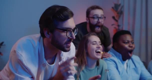 Close up of thrilled people sitting on sofa and looking at TV with excited face expression. Friends supporting team, shouting and celebrating while watching sport game at home. — Stock video