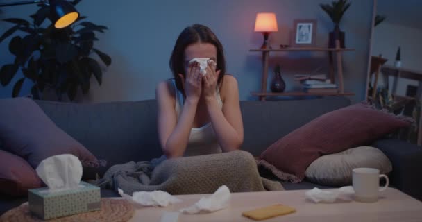 Joven infeliz milenaria llorando y usando pañuelos de papel. Mujer desesperada sentada en el sofá llorando y cubriendo la cara con las manos. Concepto de emociones y malas noticias . — Vídeos de Stock