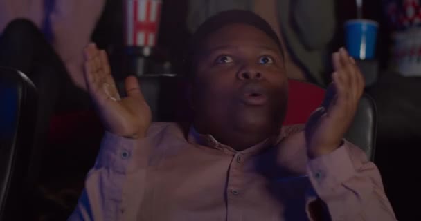 Close up of young man applauding and smiling after watching good movie in cinema. Millennial guy looking pleased with film he watching in movie theatre. People at background. — Stock video