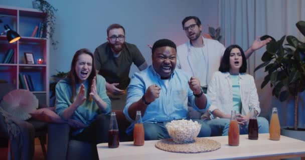 Boldog afro-amerikai srác ünnepli közel ideges barátok, miközben néz sport játék a TV-ben. Baráti társaság ül a kanapén, és támogatja a különböző csapatok sport játék. A szabadidő fogalma. — Stock videók
