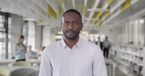 Porträtt av unga afro amerikanska kontorsarbetare tittar på kameran. Framifrån av självsäker affärsman stående i ämbetet av modernt företag. Oklar bakgrund. Begreppet arbete, människor. — Stockvideo