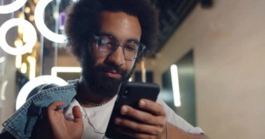 30 'lu yaşlarda ciddi bir adamın akıllı telefonuyla mesajlar yazıp sohbet ederken, gözlüklü yakışıklı sakallı bir adamın telefon ekranına bakması ve haber yayını yapması. Teknoloji kavramı.