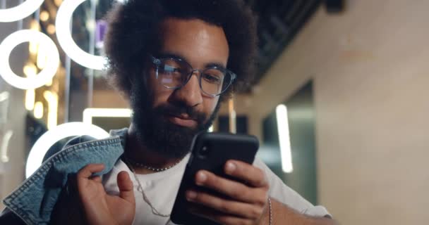 Vooraanzicht van een serieuze man in de 30 met behulp van zijn smartphone om te chatten en het typen van berichten.. Knappe bebaarde man met een bril op het scherm van de telefoon en scrollen nieuwsfeed. Concept van de technologie. — Stockvideo