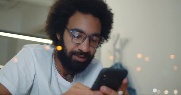 Uomo barbuto in occhiali guardando lo schermo dello smartphone e scorrendo notizie feed. Primo piano di ragazzo rilassato nel 30s utilizzando il suo cellulare per la comunicazione mentre seduto in caffè. Interni . — Video Stock