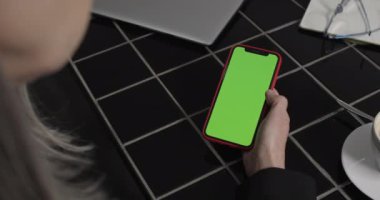 Modern akıllı telefon ve kaydırmalı ekran kullanan orta yaşlı bir kadın. Finansal haberleri okurken kadınların cep telefonlarını yeşil ekran ile tutarak ellerini kapat. İş kavramı.