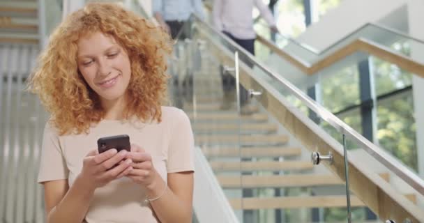 Büroangestellte mit Smartphone im Flur eines modernen Büros. Eine Angestellte eines Unternehmens surft im Netz und wischt mit ihrem Handy. Konzept von Menschen, Arbeit, Technologie. — Stockvideo