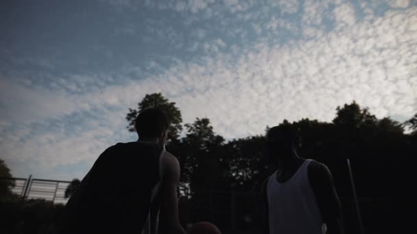 Vue de face de deux joueurs de basket-ball jouant au basket-ball, lançant le ballon vers le haut, basculant au terrain de basket-ball de rue dans la soirée. Mode de vie sain et concept sportif. Mouvement lent . — Video