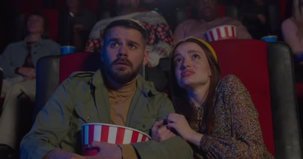 Jovem e homem assistindo thriller no cinema. Menina bonita olhar assustador enquanto assiste filme e aconchegar-se ao seu namorado sentado ao lado dela. Conceito de lazer e relacionamento . — Vídeo de Stock