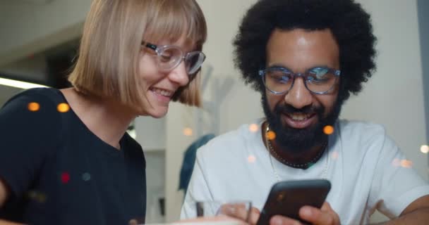 Close up de amigos felizes olhando fotos na tela do smartphone e rindo. Homem e mulher excitados se divertindo e sorrindo enquanto sentados juntos no café. Conceito de lazer . — Vídeo de Stock