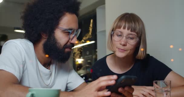 Homem e mulher sentados no café e discutindo momentos de trabalho em ambiente não formal. Duas pessoas conversando umas com as outras enquanto olham para a tela do smartphone. Conceito de comunicação e tecnologia . — Vídeo de Stock