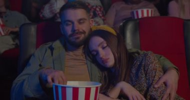 Film sırasında erkek arkadaşının omzunda uyuyan güzel bir kızın ön görüntüsü. Sakallı adam patlamış mısır yiyor, kız arkadaşına sarılıyor, ona bakıyor ve sinemaya gülümsüyor..