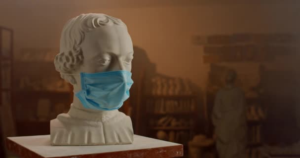 Busto de gesso branco de pessoa famosa vestindo máscara médica em pé sobre pequena mesa no estúdio escultor. Conservado da arte no qurantine . — Vídeo de Stock