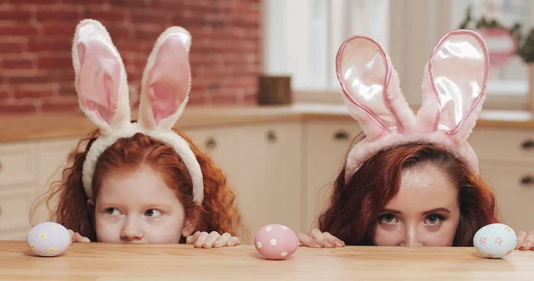 Portrait de maman drôle et sa fille portant oreille de lapin avec des œufs de Pâques regardant dans la caméra. famille heureuse s'amuser dans une cuisine confortable. Joyeuse Pâques Photo De Stock