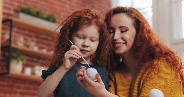 Uma mãe e sua filha pintando ovos de Páscoa na cozinha aconchegante. Eles riem e se divertem. Família feliz se preparando para a Páscoa. Feliz Páscoa. Imagens De Bancos De Imagens Sem Royalties