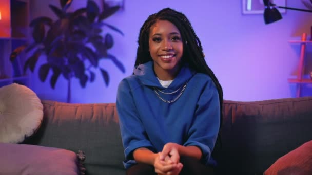 Retrato de una chica joven y guapa con ropa casual sonriendo mientras mira a la cámara. Alegre mujer milenaria con rastas posando a la cámara mientras está sentado en el sofá en casa.Ampliar . — Vídeos de Stock