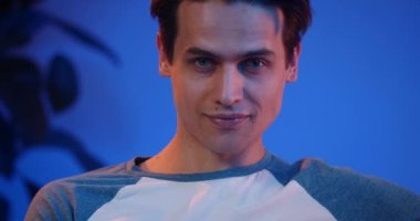 Yakışıklı genç adam kameraya bakıyor ve poz veriyor. Gündelik giysiler içinde, kafa kaldıran ve gülümseyen sevimli bir milenyum erkeğinin yakın görüntüsü. Yaşam tarzı ve eğlence anlayışı. Ev arkaplanı.