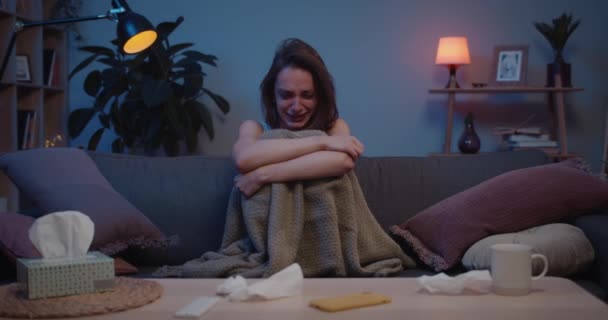 眼前的景象是一个悲伤的女孩一个人坐在房间的沙发上，抱着膝盖。年轻不快乐的女人因为感情问题和手牵着手哭泣。感情的概念. — 图库视频影像