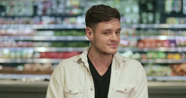 Portret van een knappe jongen die zijn hoofd draait en glimlacht naar de camera. Moderne duizendjarige man poseren terwijl hij in de supermarkt staat. Concept van winkelen en het echte leven. Wazige achtergrond. — Stockvideo