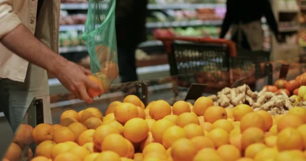 Vista da colheita de cara colocando laranjas em saco de produtos reutilizáveis. Homem caucasiano fazendo compras no departamento de frutas e legumes no supermercado. Conceito de vida real e estilo de vida ecológico . — Vídeo de Stock