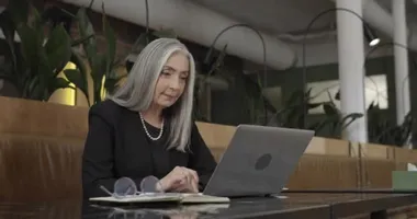 Laptopta iş sunumunu izleyen olgun, zarif bir kadın CEO yöneticisi. Kafede otururken bilgisayarla çalışan orta yaşlı güzel bir iş kadınının yan görüntüsü. Kapalı.