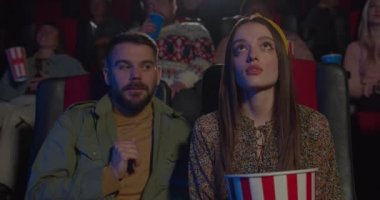 Sinemada film izlerken genç bir kadını kucaklayan yakışıklı bir adam. Romantik çiftin sinemada buluşup film izlemesi ön planda. Boş zaman ve ilişki kavramı.