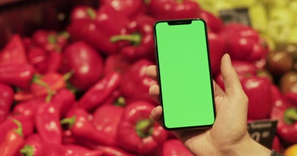 Nahaufnahme des händchenhaltenden Smartphones und des grünen Bildschirms im Supermarkt. Rote Klingelschilder auf verschwommenem Hintergrund. Konzept des Einkaufs, Chroma-Schlüssel und Attrappe. — Stockvideo