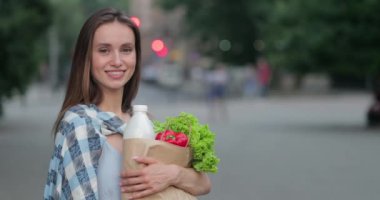 Gülümseyen ve kameraya bakan güzel yüzlü bir kadının portresi. Elinde yiyecek ve poz veren neşeli bir kız sokakta dikilirken. Sağlıklı beslenme kavramı. Yakınlaştır.