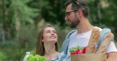 Yiyecek dolu çantalar taşıyan ve birlikte iyi vakit geçiren mutlu çiftlere yakın durun. Gözlüklü sakallı adam kız arkadaşına sarılıyor ve onu öpüyor..