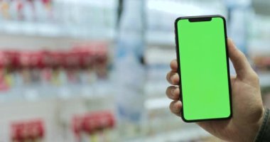 Erkek elinin modern cep telefonuyla ekranı dikey modda taklit edişinin yakın görüntüsü. Krom anahtar ve yeşil ekran kavramı. Arka plan bulanık. Kapalı.