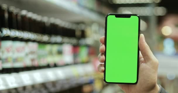 Vista de perto da mão masculina segurando smartphone moderno com tela verde no supermercado. Conceito de simular e tecla chroma. Fundo desfocado . — Vídeo de Stock