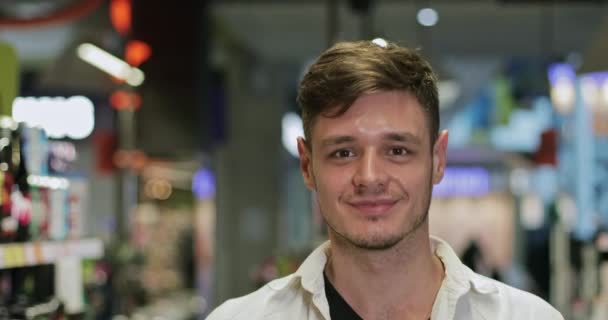 Vue rapprochée du jeune homme joyeux regardant vers la caméra tout en marchant à la section des boissons gazeuses. Portrait de heureux gars milléniaux souriant dans la boutique. Concept de shopping et de vie réelle . — Video