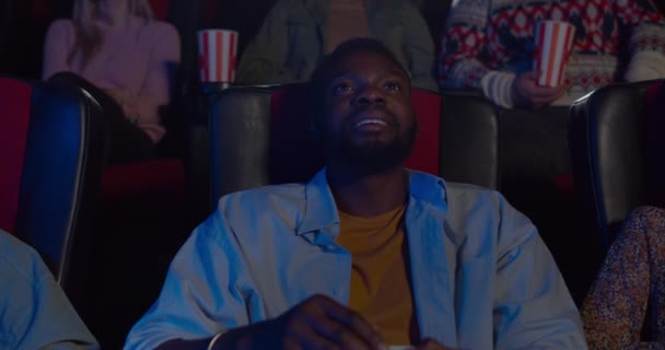 Primer plano del chico guapo viendo películas de acción en el cine. Hombre africano joven haciendo grandes ojos y la boca abierta en el cine. Concepto de entretenimiento y emociones de la gente . — Vídeos de Stock