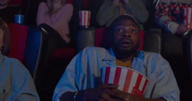 Genç yakışıklı adam filmdeki korkunç ana tepki veriyor. Sinemada horor film izleyen ve patlamış mısır kasesine sarılan Afrikalı adam. Eğlence ve eğlence anlayışı.