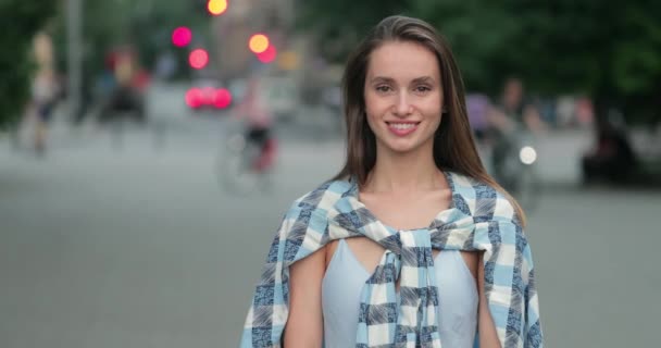 Beskär utsikt över vackra glad kvinna tittar till kameran när du står på gatan. Porträtt av attraktiv flicka i avslappnade kläder poserar till kameran och ler. Begreppet verklighet. — Stockvideo