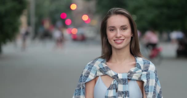 Radosna tysiącletnia kobieta patrząca w kamerę stojąc na ruchliwej ulicy. Portret pięknej dziewczyny w ubraniu casual pozowanie i uśmiech do kamery. Powiększ. Pojęcie prawdziwego życia. — Wideo stockowe