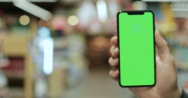 Kişinin modern akıllı telefonu tutup ekranı dikey kipte taklit ettiği görüntüyü kapat. Krom anahtar ve yeşil ekran kavramı. Arka plan bulanık. Kapalı.