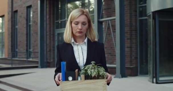 Smutna kobieta po trzydziestce trzymająca pudełko z rzeczami podczas zwolnienia z pracy. Kobieta wyglądająca na nieszczęśliwą podczas spaceru z rzeczami na ulicy. Pojęcie bezrobocia. — Wideo stockowe