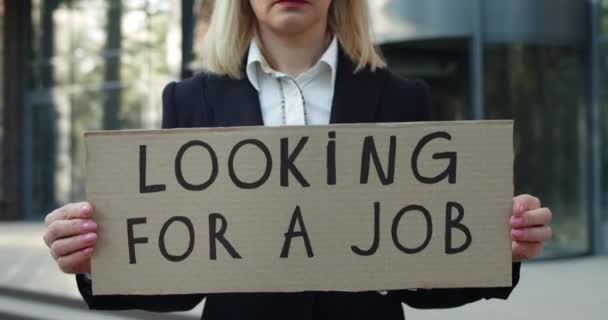 Oříznout pohled na zaměstnankyni bez práce po uzamčení pandemie. Žena ve 30s ukazující karton s hledáním práce psaní, zatímco stojí na ulici a dívá se do kamery. — Stock video