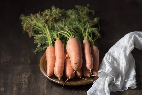 natural carrot on clay plate, on a wooden board, next to a razor and a dishcloth, on dark background