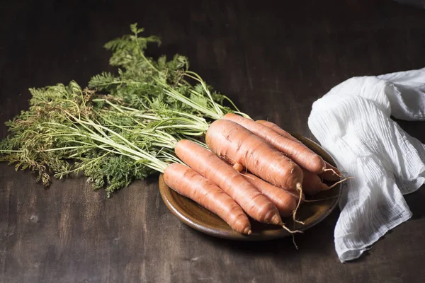 natural carrot on clay plate, on a wooden board, next to a razor and a dishcloth, on dark background