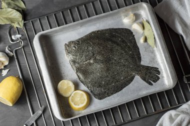 Fırında pişirilmeye hazır sarımsak, limon ve defne yaprağıyla fırın tepsisi üzerinde turbot.