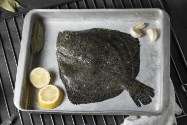 Turbot on a baking sheet and oven rack, with garlic, lemon and bay leaf, prepared to be baked in the oven clipart