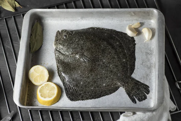 Turbot on a baking sheet and oven rack, with garlic, lemon and bay leaf, prepared to be baked in the oven