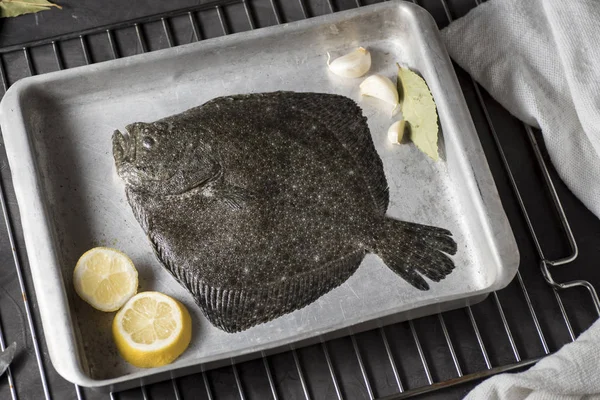 Turbot on a baking sheet and oven rack, with garlic, lemon and bay leaf, prepared to be baked in the oven
