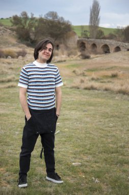 Tarlada poz veren ve arka planda köprüsü olan genç bir adam. Açık havanın tadını çıkarıyorum.