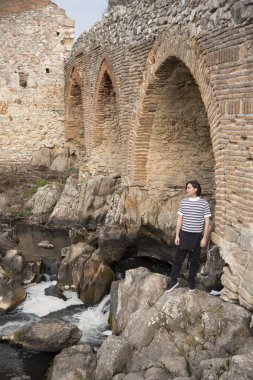 Tarlada poz veren ve arka planda köprüsü olan genç bir adam. Açık havanın tadını çıkarıyorum.